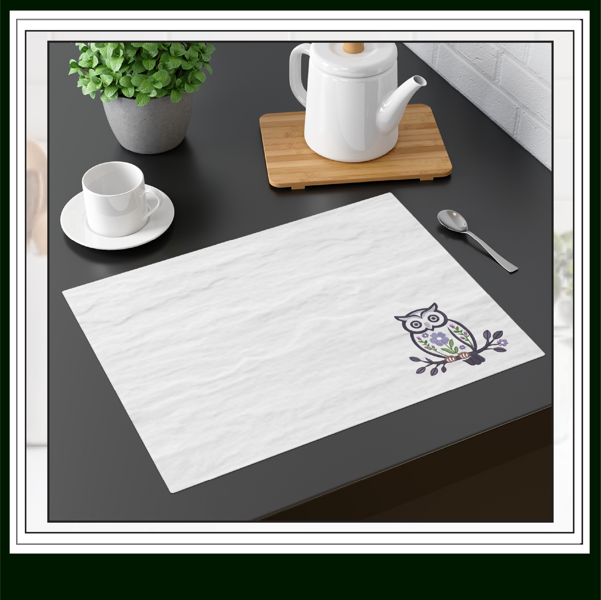 White placemat with owl design on a kitchen counter with tea set and plant.