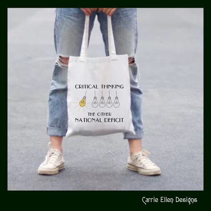 Tote bag with 'Critical Thinking: The Other National Deficit' text and light bulb graphics, held by a person wearing ripped jeans and white sneakers.